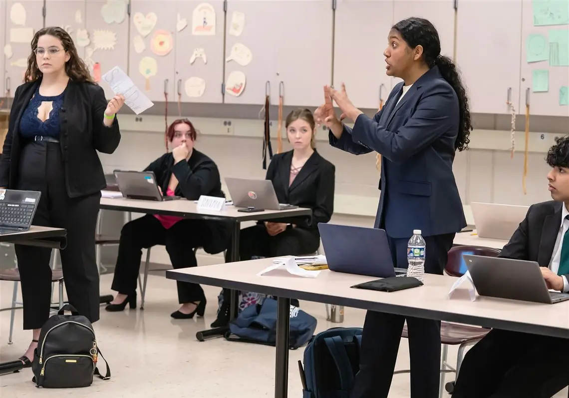 Students debating in a classroom while a judge takes notes